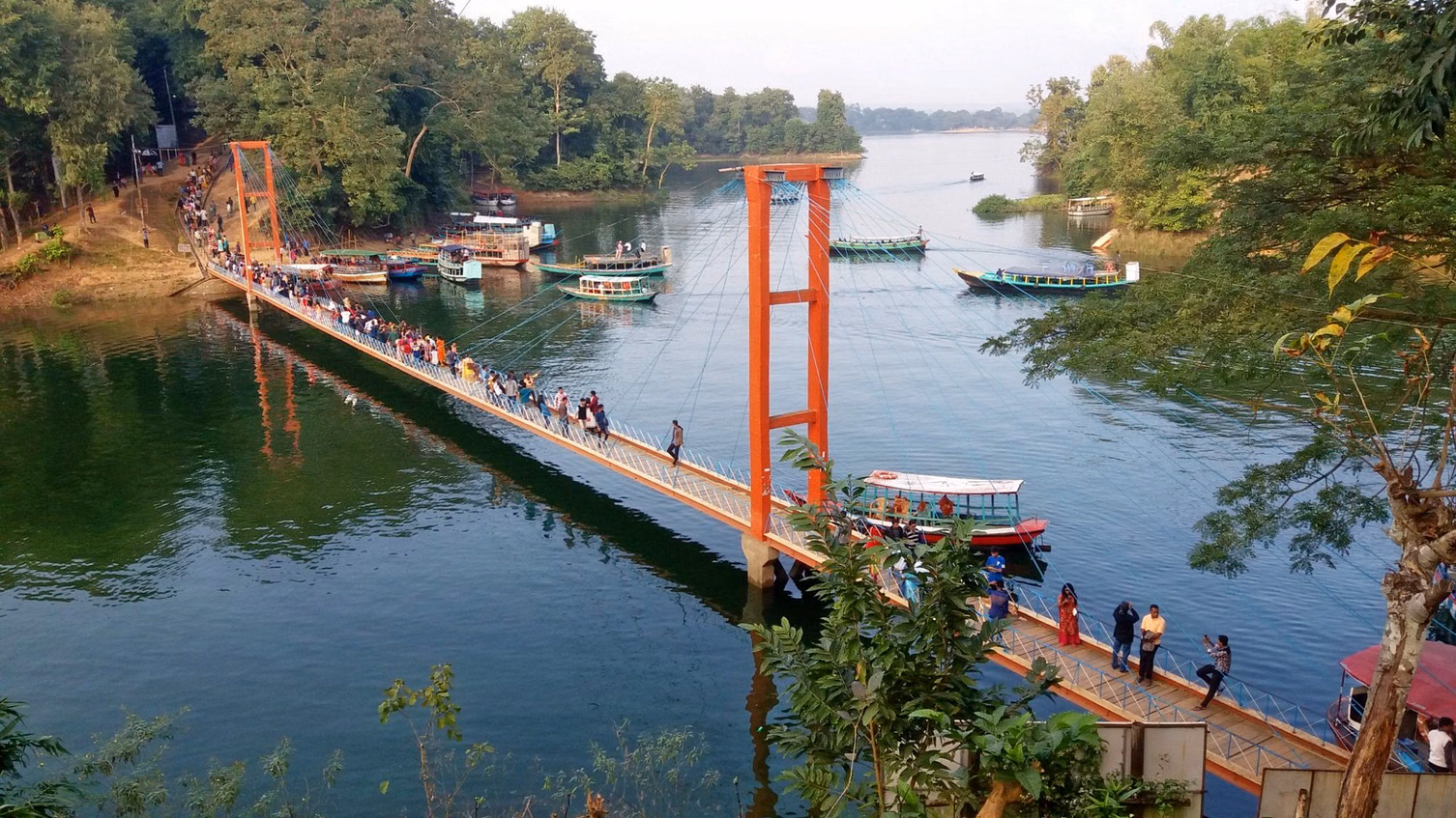 A footbridge over a calm lake with moored boats and forested banks